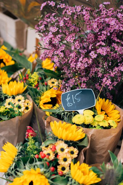 An assortment of fresh flower bouquets displayed outdoors, featuring vibrant yellow sunflowers, small white daisies with yellow centers, and red and pink blossoms arranged in brown craft paper wrappin